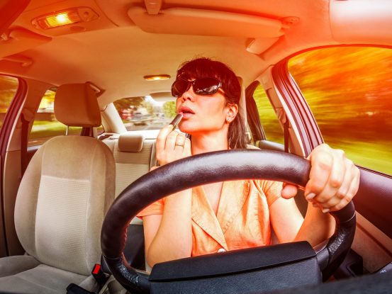 Image of a woman putting lipstick on her lips while at the wheel of a car