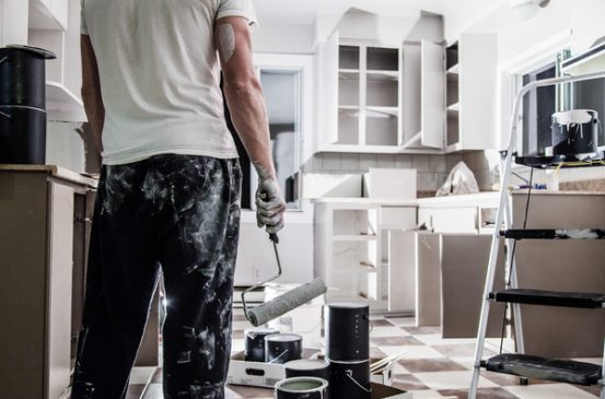 Image of man from behind standing in front of a freshly painted white kitchen with paint roller in hand